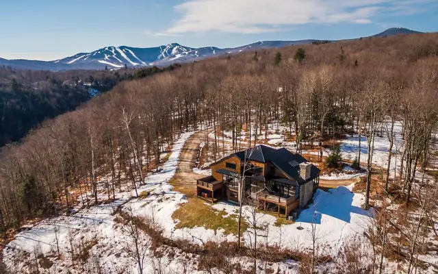 Aerial view of a mountain home on a wooded hillside with ski trails beyond